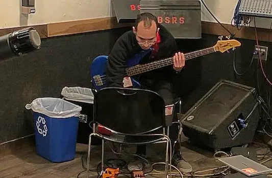 me recording the bass part of a song in a studio surrounded by audio equipment looking down at a laptop