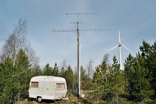 giant wooden post with giant multi-element antenna outside of a small camper in the middle of the woods